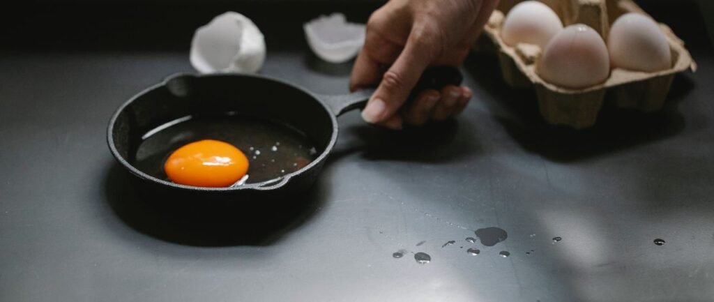 Crop faceless female preparing delicious traditional fried eggs in pan in kitchen at home